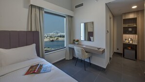 Ein Hotelzimmer mit Bett, Schreibtisch, Stuhl, einer kleinen Küchenzeile und Blick auf eine Brücke und Wasser.