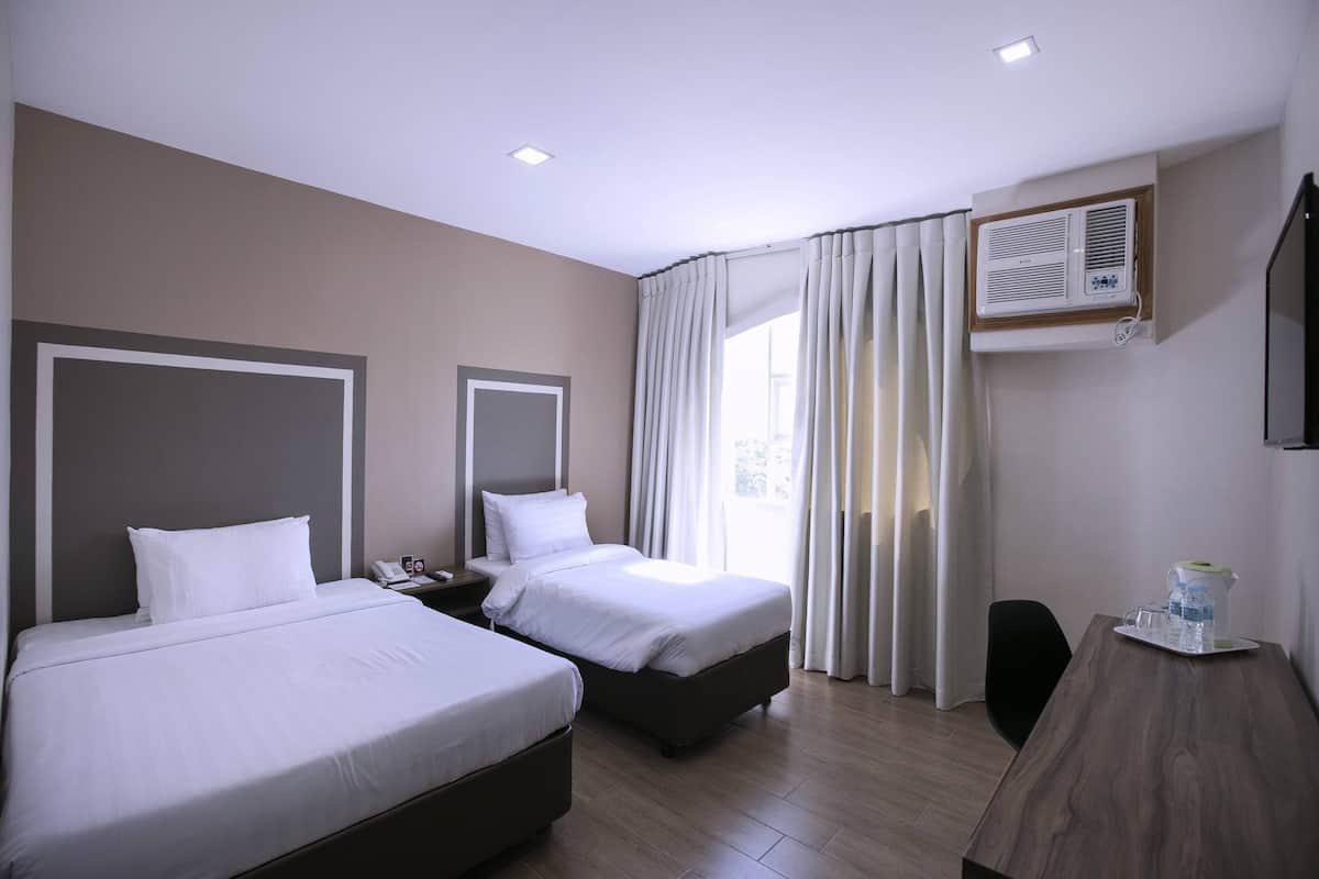 A hotel room with two beds, a desk, a chair, and a window with curtains.