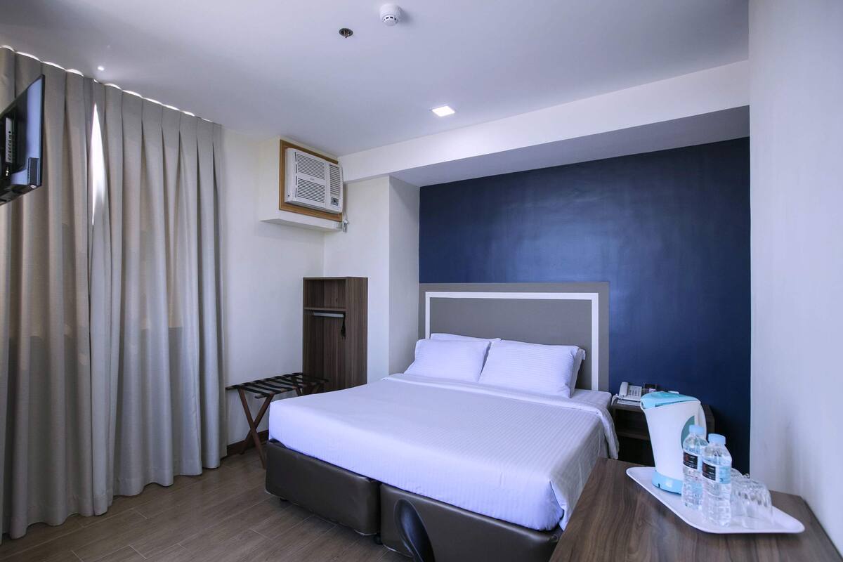 A hotel room with a bed, a desk, a chair, a TV, a wardrobe, and a window with curtains.