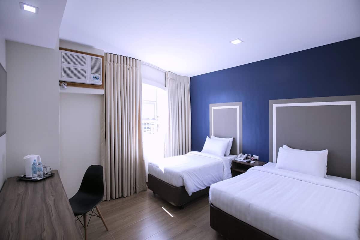 A hotel room with two beds, a desk, a chair, and a window with curtains.