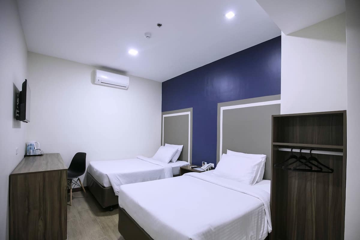 A hotel room with two single beds, a desk, a chair, a wardrobe, and a TV.