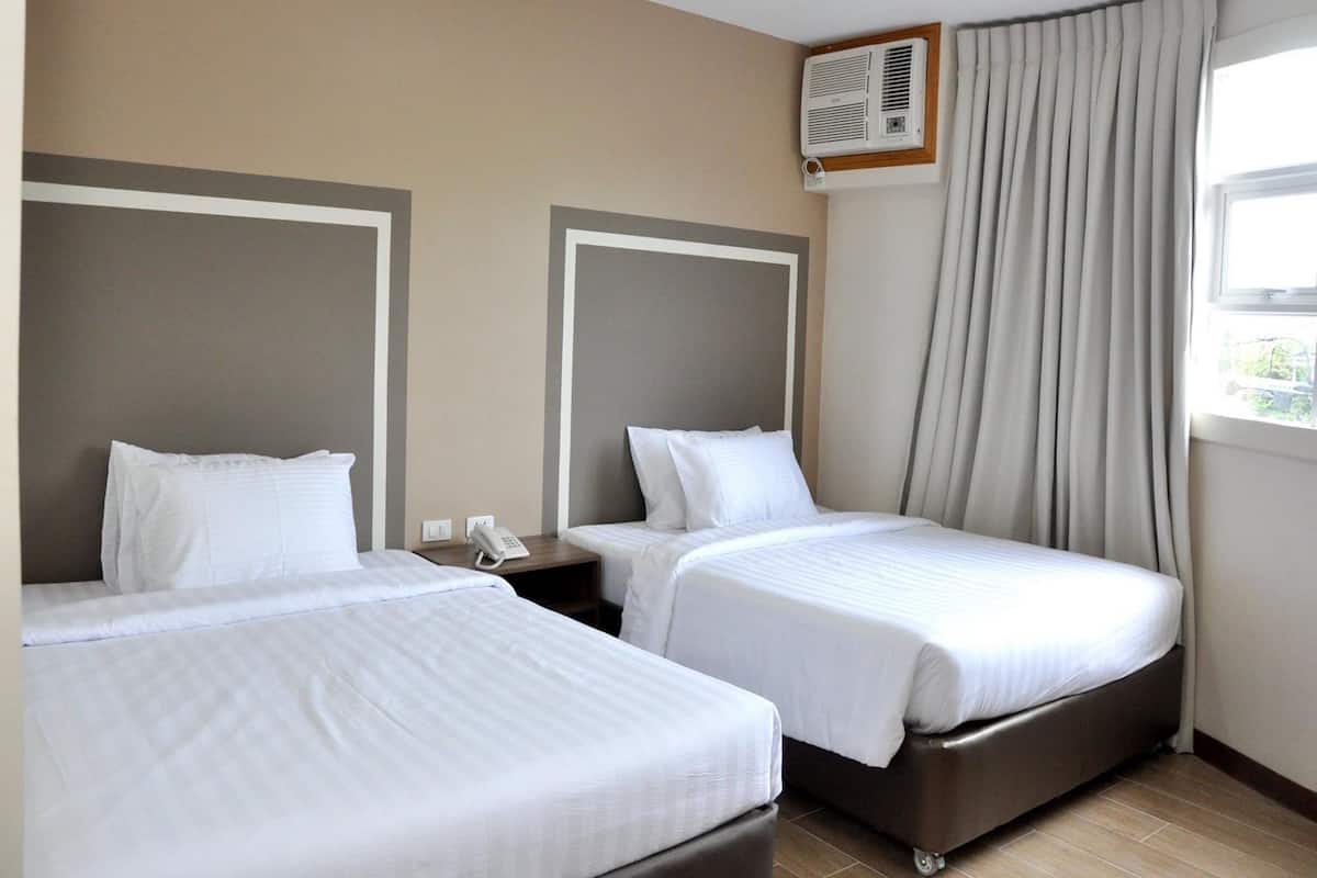 A hotel room with two beds, a telephone, an air conditioning unit, and a window with curtains.