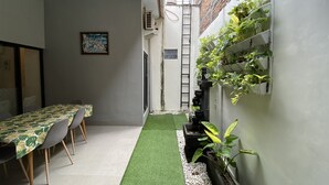 Un couloir étroit avec une table et des chaises, un petit espace jardin agrémenté de galets blancs et un jardin vertical sur le mur de droite.