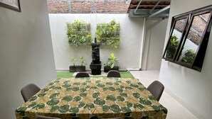 Un espace repas avec une table recouverte d’un motif de feuilles tropicales, entourée de chaises. On y trouve des plantes en pot sur un jardin vertical et un escalier menant à un niveau supérieur.