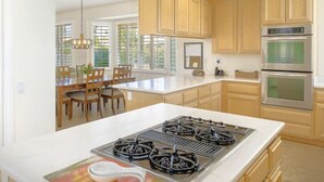 A modern kitchen with wooden cabinets, a central island, a gas stove, and built-in ovens. - Spanish Mission in Gated Private Golf Club (Palm Desert)