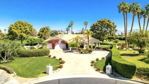 A two-story house with a central driveway, surrounded by well-maintained lawns and palm trees. - Spanish Mission in Gated Private Golf Club (Palm Desert)