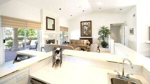 A modern kitchen with a central island, a dining area with a sofa, and a large window offering a view of the outdoors. - Spanish Mission in Gated Private Golf Club (Palm Desert)