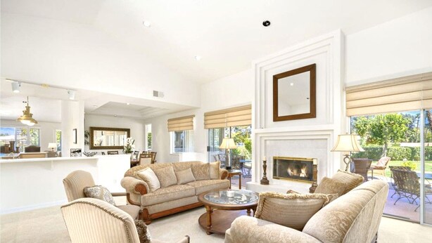 A spacious living room with a fireplace, comfortable seating, and large windows offering a view of the outdoors. - Spanish Mission in Gated Private Golf Club (Palm Desert)