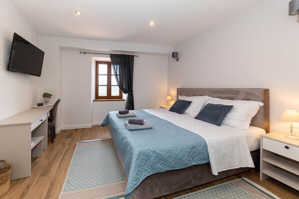 A bedroom with a bed, bedside tables, a desk, a TV, and a window with curtains.