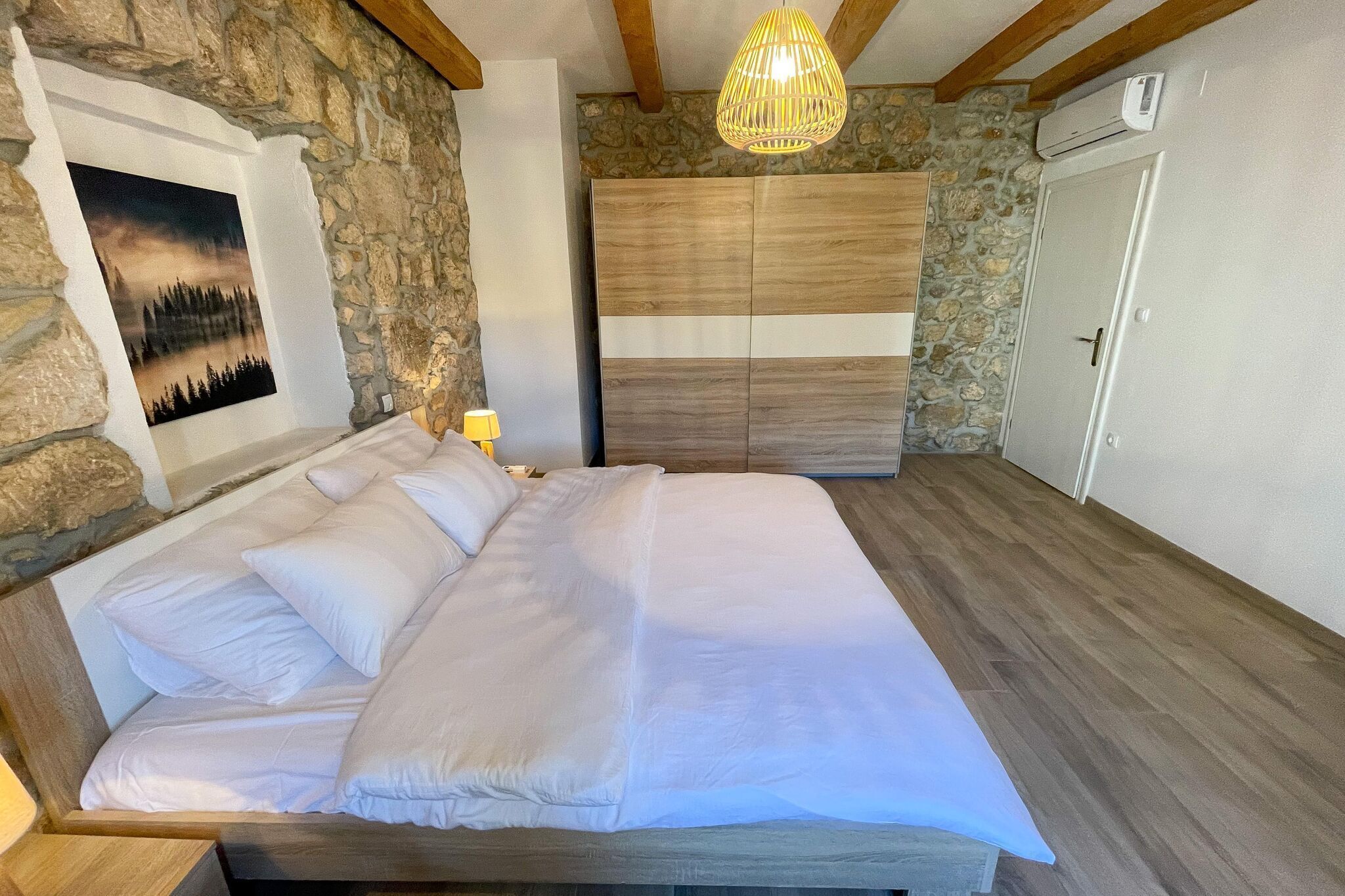 A bedroom with a large bed, stone walls, a wooden ceiling, and a hanging light fixture.
