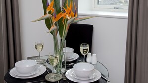 A dining table set with white bowls, plates, and glasses, accompanied by a vase of orange and purple flowers. - Stunning 2 Bed Waterfront Apartment in Media City (Salford)
