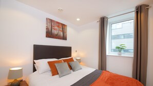 A neatly made bed with a white and orange bedspread, a dark headboard, and two bedside lamps. - Stunning 2 Bed Waterfront Apartment in Media City (Salford)