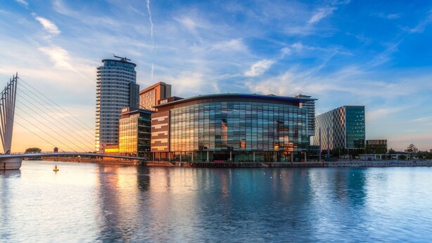 A modern building with a glass facade, a bridge in the background, and a body of water in the foreground. - Stunning 2 Bed Waterfront Apartment in Media City (Salford)