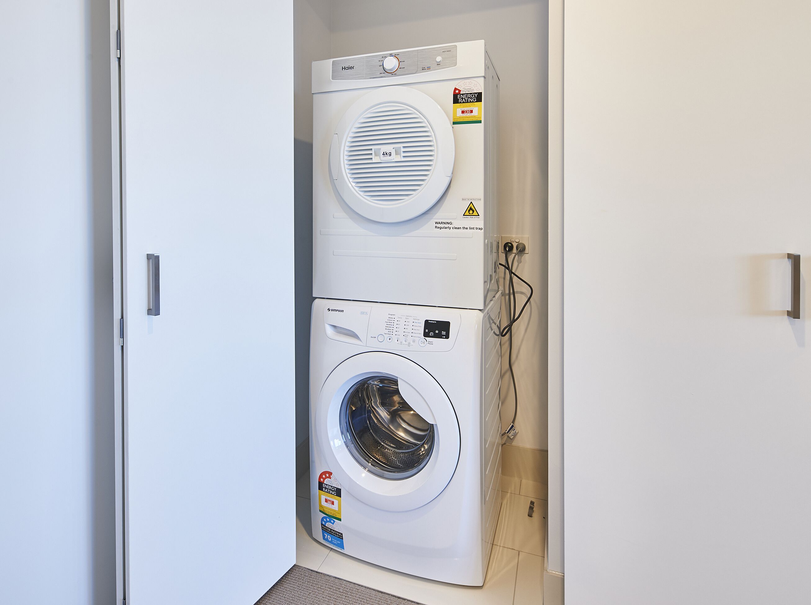 Une buanderie équipée de deux machines à laver superposées, une de marque Haier et l’autre de marque Simpson, toutes deux munies d’étiquettes indiquant leur classe d’efficacité énergétique.