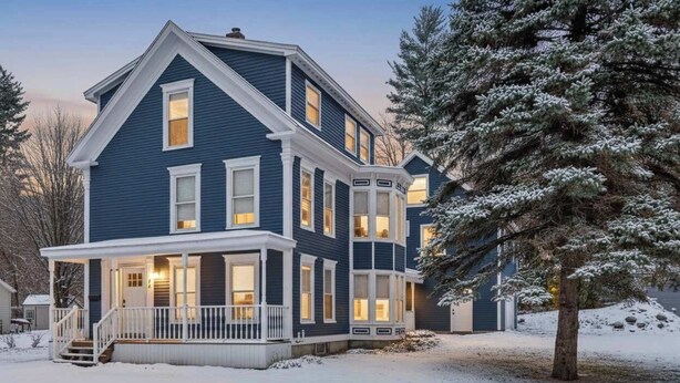 A two-story house with a porch, large windows, and a snow-covered landscape.