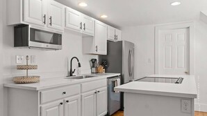 A modern kitchen with white cabinets, a stainless steel microwave, a refrigerator, and a dishwasher.