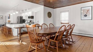 Un comedor amplio con una mesa y sillas de madera, una cocina al fondo y un ventilador de techo.