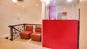 Una zona de recepción con mostrador rojo, barandilla de metal negro y dos sillones de cuero.