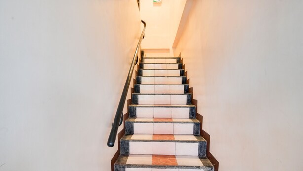 Una escalera con peldaños alternados en blanco y marrón, una barandilla de metal y una luz en la parte superior.