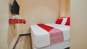 Habitación de hotel con cama, manta roja y blanca estampada, almohada roja, almohada blanca, teléfono rojo y televisor montado.