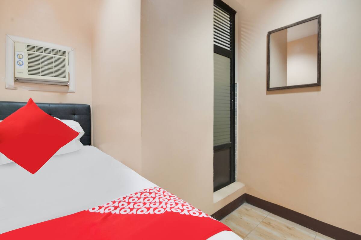 Une chambre d’hôtel avec un lit, une fenêtre avec des stores, un climatiseur fixé au mur et un miroir.