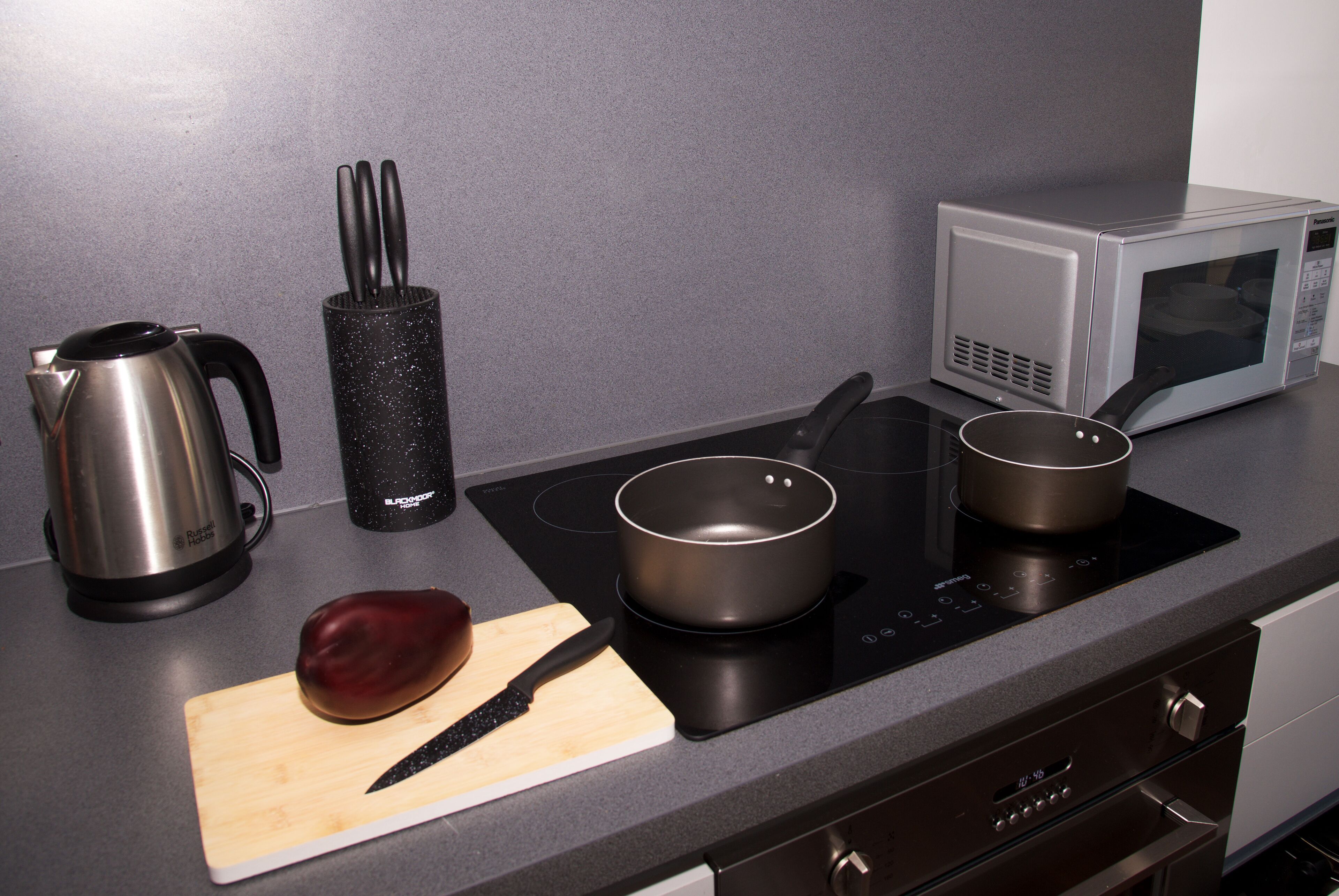 Une cuisine équipée d’une cuisinière, d’un four à micro-ondes, d’une bouilloire, d’un couteau et d’une planche à découper avec une aubergine.
