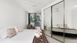 Een moderne hotelkamer met een groot bed, een bank, een glazen scheidingswand en een plafondventilator.