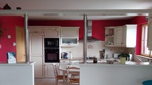 A kitchen with white cabinets, a microwave, oven, and a dining area with chairs and a table. - Spacious house with enclosed garden in Sainte-Mère-Église, pets allowed (Sainte-Mère-Église)