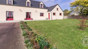 A two-story house with a red door and windows, a paved driveway, and a well-maintained lawn. - Spacious house with enclosed garden in Sainte-Mère-Église, pets allowed (Sainte-Mère-Église)
