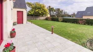 A residential property with a paved patio, a red door, and a well-maintained lawn. - Spacious house with enclosed garden in Sainte-Mère-Église, pets allowed (Sainte-Mère-Église)