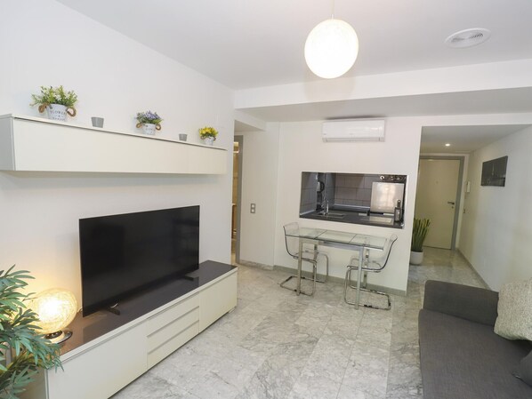 A modern living room with a flat-screen TV, a glass dining table, and a kitchen area with a built-in oven and sink. - Modern Apartment with Terrace, A/C, and WiFi in Central Salou (Salou)