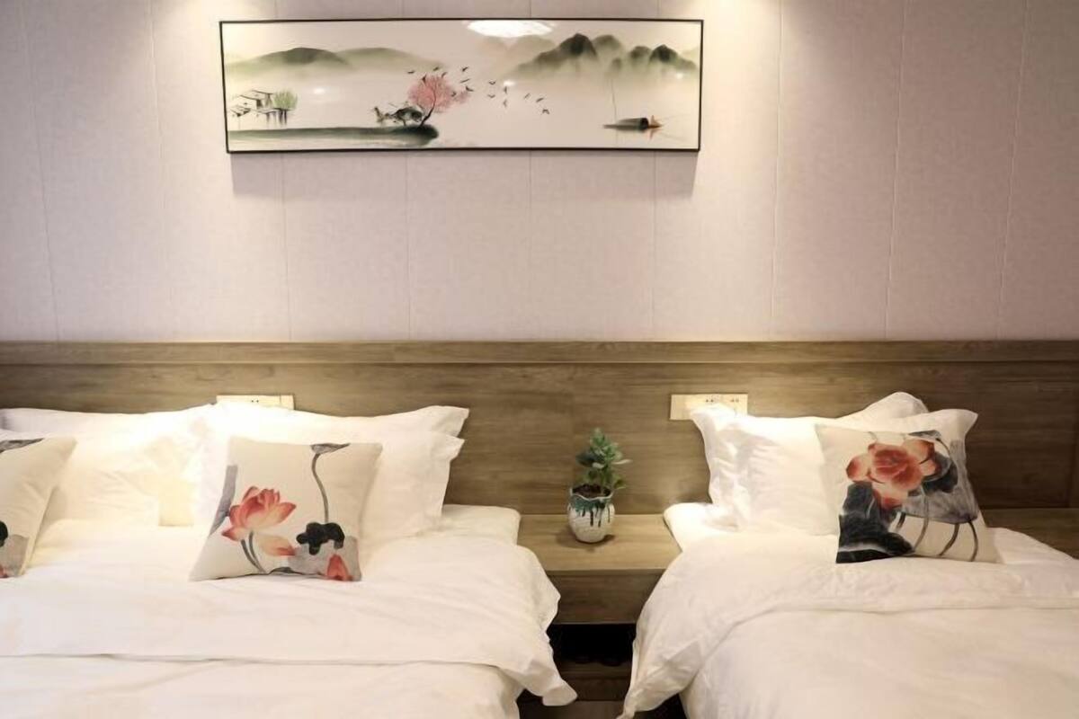 A hotel room with two beds, each with floral pillows, a small potted plant, and a framed artwork above the beds.