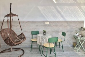 Une piÚce avec un fauteuil suspendu, une table ronde entourée de chaises et une petite plante posée sur la table.