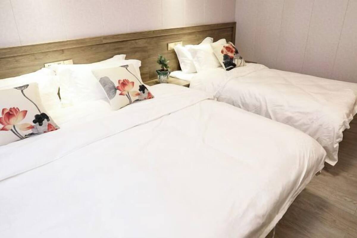 A hotel room with two beds, each with white bedding and floral-patterned pillows.