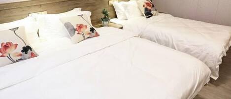 A hotel room with two beds, each with white bedding and floral-patterned pillows.