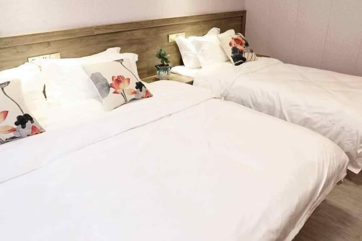 A hotel room with two beds, each with white bedding and floral pillows.