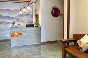 Un mostrador de recepción con un mural, un banco de madera y un objeto circular rojo en la pared.