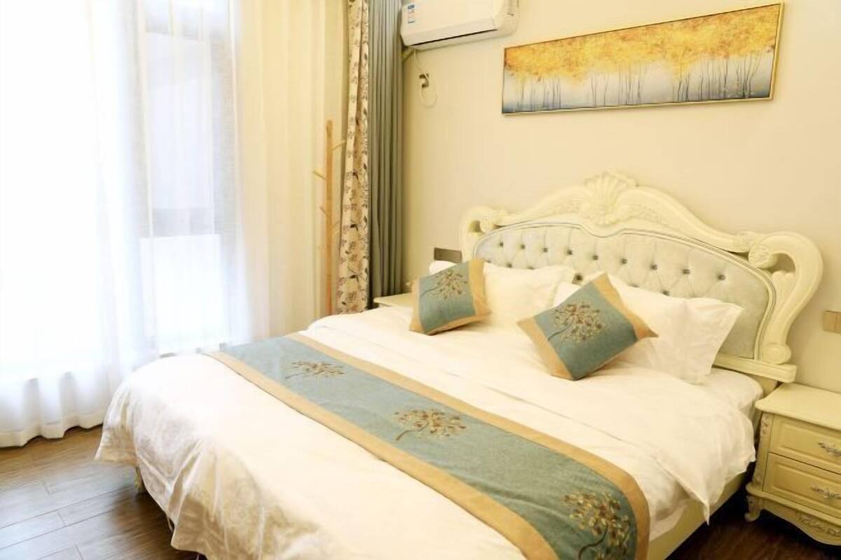 A bedroom with a bed, curtains, a painting, and a nightstand.
