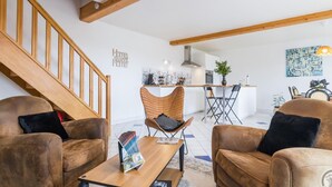 A spacious living area with a wooden staircase, a dining table with chairs, and a kitchen in the background. - Cozy house with enclosed garden and terrace in Canville-la-Rocque (Canville-la-Rocque)
