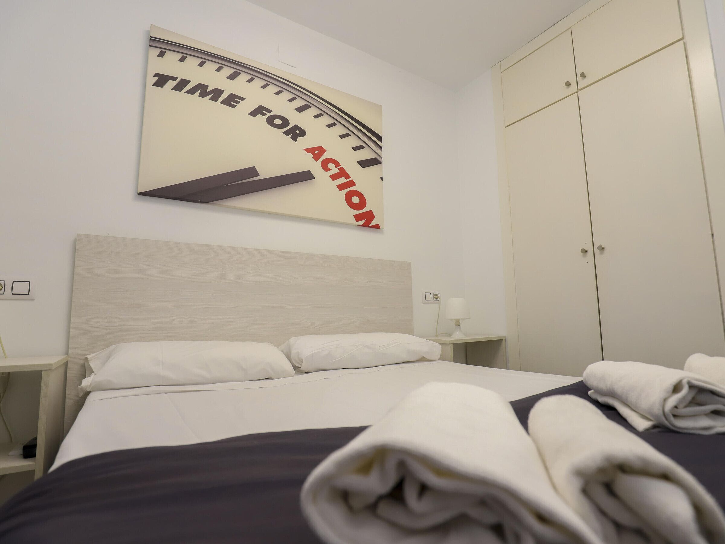 Une chambre d’hôtel comprenant un lit, une table de chevet, une horloge murale et une armoire.