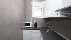 Een kleine keuken met een magnetron, een koffiezetapparaat, een spoelbak en een raam boven het aanrecht.