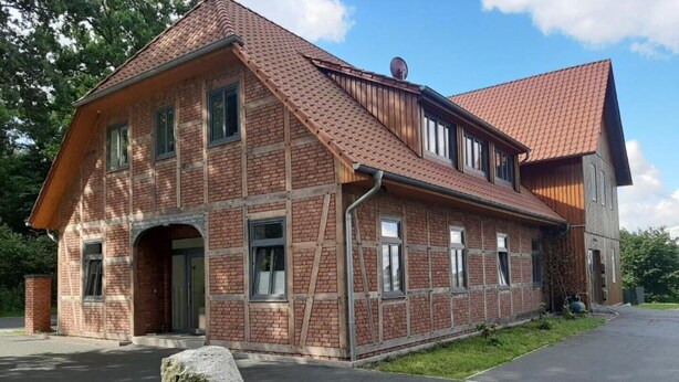 Un bâtiment en briques de deux étages, doté d’un toit en pente, de grandes fenêtres et d’un pilier en pierre en premier plan.