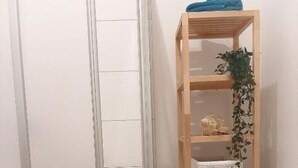 Une pièce avec une étagère en bois adossée à un mur blanc, une porte dotée d’une poignée en métal et un plancher en bois.