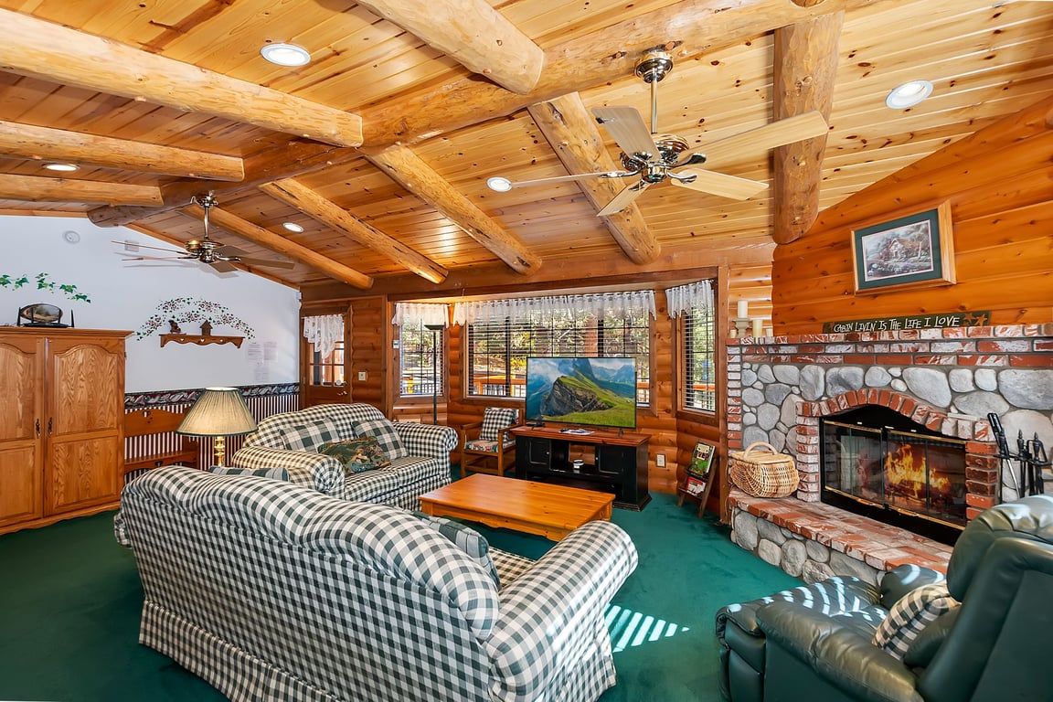 Ein Blockhaus-Interieur mit Kamin aus Stein, karierten Sofas und einem Fernseher.