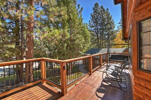 A wooden deck with a railing, surrounded by tall pine trees.