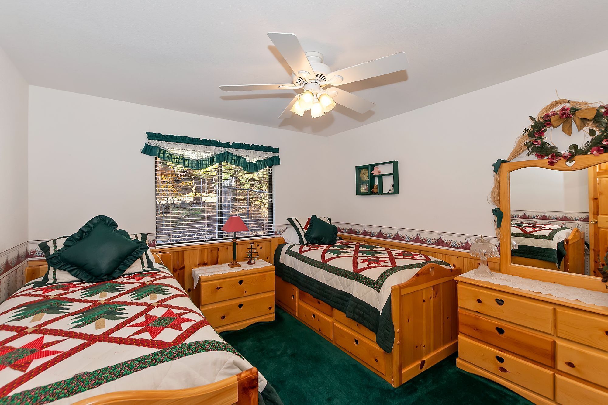 A bedroom with two wooden beds, a ceiling fan, a window with blinds, a mirror, and a dresser.