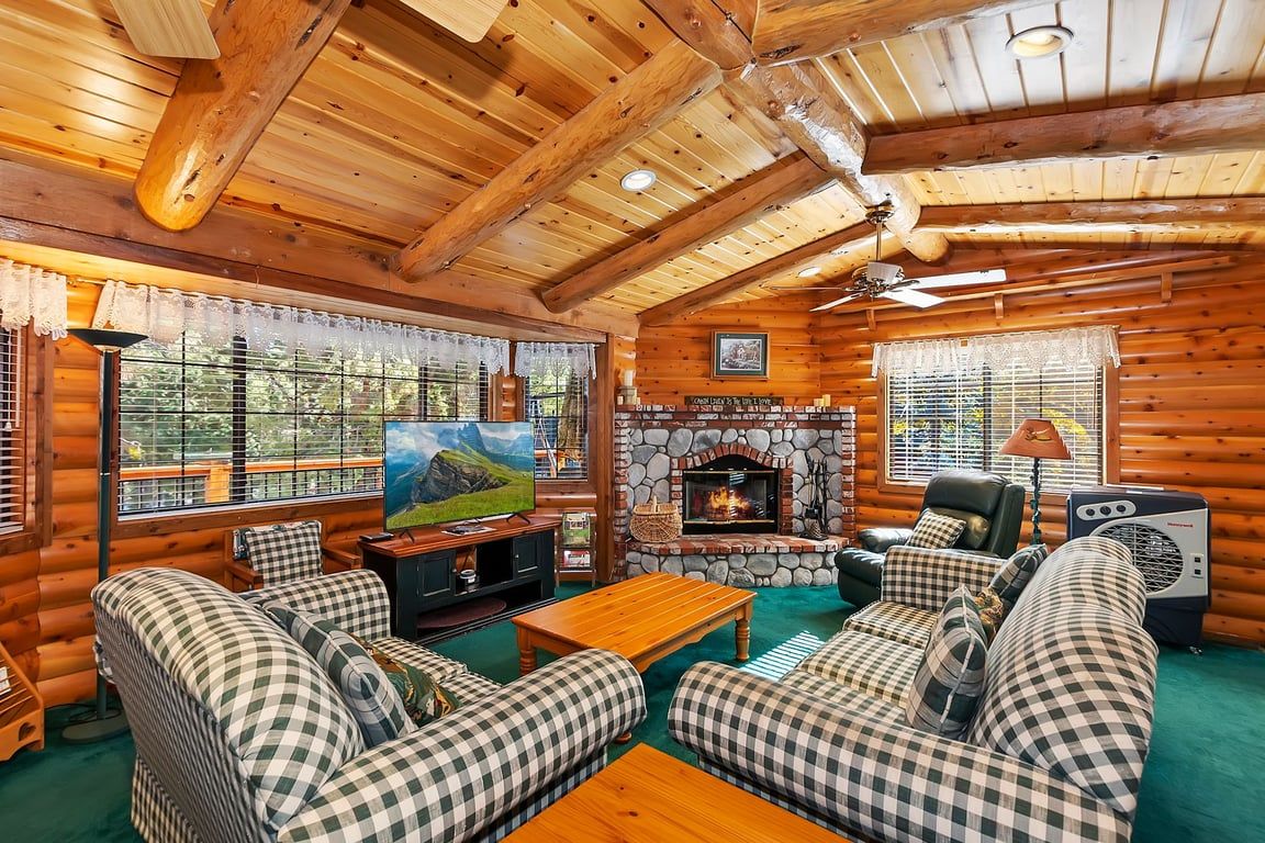 A log cabin interior with a stone fireplace, checkered sofas, a television, and a ceiling fan.