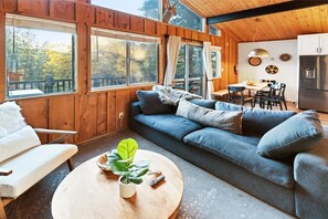 A cozy cabin interior with a sofa, a dining table, and a kitchen area.
