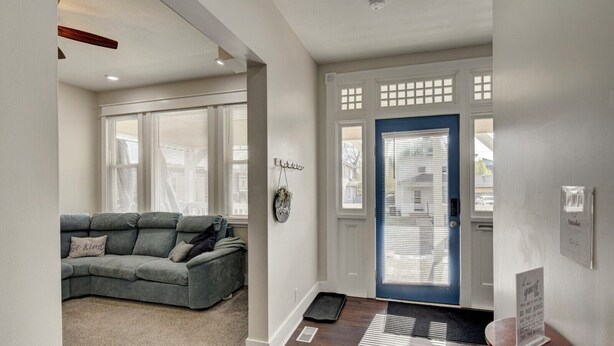 A modern living room with a grey sectional sofa, a wooden ceiling fan, and a blue door with a decorative window grille. - 1890's Craftsman Home 5BR 4BA, Sleeps 16+ w 6 TVs. (Omaha)