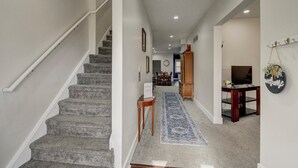 A staircase leading to a landing with a blue patterned rug, a wooden cabinet, and a welcome sign. - 1890's Craftsman Home 5BR 4BA, Sleeps 16+ w 6 TVs. (Omaha)